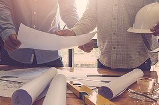 Two men standing near a table looking over project blueprints